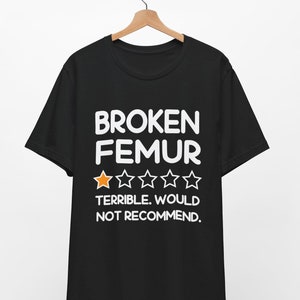 May include: Black t-shirt with the words "BROKEN FEMUR" in white block letters. Below the text is a rating of one out of five stars, and the words "TERRIBLE. WOULD NOT RECOMMEND."