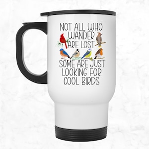 May include: White travel mug with a black handle and black bottom. The mug has a black and white graphic of birds with the text "Not all who wander are lost. Some are just looking for cool birds."