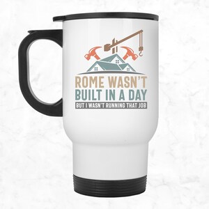 May include: White travel mug with a black handle and lid. The mug features a graphic of a house under construction with the text "Rome wasn't built in a day, but I wasn't running that job."