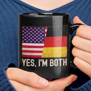 May include: Black coffee mug with a white and red American flag and a black, red, and yellow German flag on the front. The text "YES, I'M BOTH" is printed below the flags.