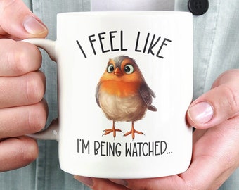 Könnte beinhalten: Eine weiße Keramiktasse mit einer Schwarzweißillustration eines Rotkehlchens mit dem Text "I feel like I'm being watched..."