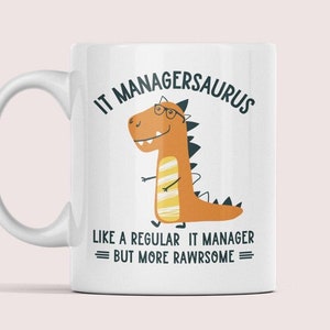 Könnte beinhalten: Weiße Keramiktasse mit einem Comic-Dinosaurier, der eine Brille trägt, und dem Text "IT MANAGERSAURUS LIKE A REGULAR IT MANAGER BUT MORE RAWRSOME".