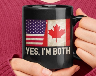 Puede incluir: Una taza de café negra con una bandera estadounidense blanca y roja y una bandera canadiense en un lado y el texto "YES, I'M BOTH" en el otro.