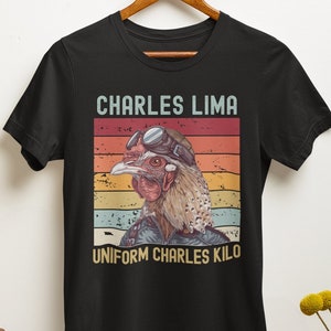 May include: Black t-shirt with a retro-style graphic of a chicken wearing aviator goggles and a pilot's uniform. The text "CHARLES LIMA UNIFORM CHARLES KILO" is printed below the image.