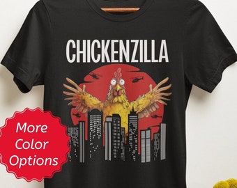 May include: Black t-shirt with a graphic of a chicken with its wings spread wide, standing in front of a city skyline with a red sun behind it. The text "CHICKENZILLA" is printed above the chicken.