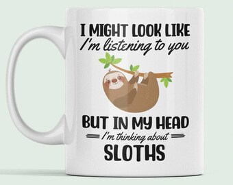 May include: White ceramic mug featuring a black and brown sloth illustration. The mug reads "I might look like I'm listening to you but in my head I'm thinking about sloths."