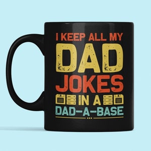 May include: Black coffee mug with a white design that says "I keep all my dad jokes in a dad-a-base".