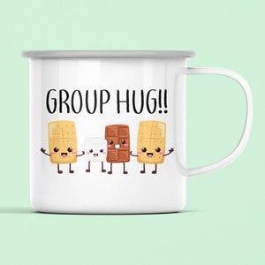Może przedstawiać: Biały emaliowany kubek do campingu z czarno-białym rysunkiem krakersa, pianki i tabliczki czekolady trzymających się za ręce. Tekst "GROUP HUG!" jest nadrukowany nad rysunkiem.