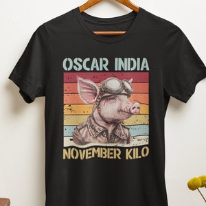 May include: Black t-shirt with a vintage-style graphic of a pig wearing aviator goggles and a leather jacket. The text "OSCAR INDIA NOVEMBER KILO" is printed below the pig.