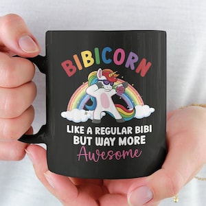 May include: Black coffee mug with a white unicorn wearing sunglasses and a rainbow behind it. The text on the mug reads "Bibicorn Like a regular bibi but way more Awesome".