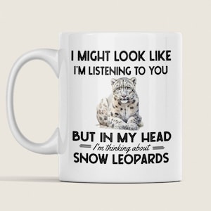 May include: White ceramic mug featuring a black and white image of a snow leopard. The mug reads "I might look like I'm listening to you, but in my head I'm thinking about snow leopards."