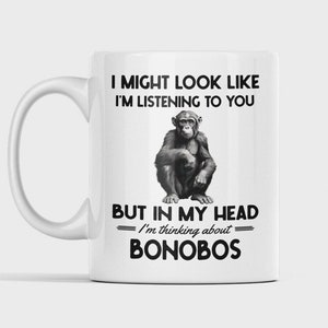 May include: White ceramic mug with a black and white image of a chimpanzee. The mug has the text "I might look like I'm listening to you, but in my head I'm thinking about bonobos."