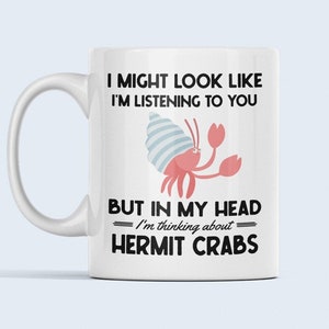 May include: White ceramic mug with a black and white graphic of a hermit crab. The text reads "I might look like I'm listening to you, but in my head I'm thinking about hermit crabs."