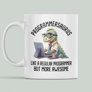 May include: White ceramic mug with a green dinosaur wearing glasses and typing on a laptop. The text on the mug reads "Programmersaurus Like a regular programmer but more awesome."