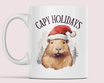 Può includere: Tazza in ceramica bianca con un'illustrazione ad acquerello di un capibara con un cappello da Babbo Natale. La tazza presenta la scritta "CAPY HOLIDAYS" in bordeaux. Lo sfondo include una scena di foresta innevata.