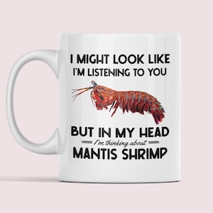 May include: White ceramic mug with a black and white graphic of a mantis shrimp. The text on the mug reads "I might look like I'm listening to you, but in my head I'm thinking about mantis shrimp."