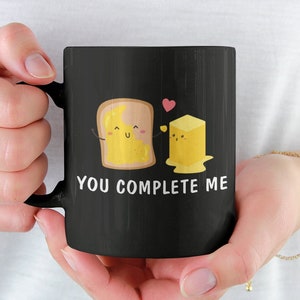 Può includere: Tazza da caffè nera con una grafica bianca di una fetta di pane e un pezzo di burro con il testo "You Complete Me".