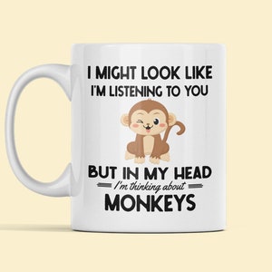 May include: White ceramic coffee mug with a black and brown illustration of a monkey. The text on the mug reads "I might look like I'm listening to you but in my head I'm thinking about monkeys."