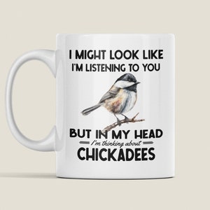 May include: White ceramic mug with a black and white illustration of a chickadee bird. The text on the mug reads "I might look like I'm listening to you, but in my head I'm thinking about chickadees."