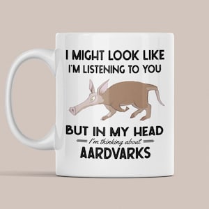 Op de afbeelding: Een witte keramische mok met een zwart-bruine illustratie van een aardvarken. Op de mok staat "Ik kan eruit zien alsof ik luister, maar in mijn hoofd denk ik aan aardvarkens."
