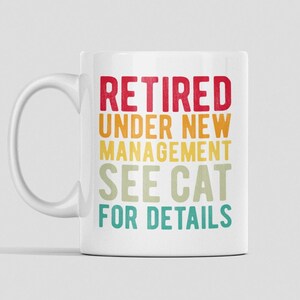 以下が含まれることがあります： レトロなフォントでカラフルなアクセントが付けられた「Retired under new management see cat for details」というテキストが書かれた白いセラミック製のコーヒーカップです。