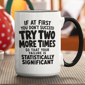 Peut inclure: Un mug en céramique blanche avec une anse et un bord noirs, portant le texte imprimé en noir : IF AT FIRST YOU DON'T SUCCEED TRY TWO MORE TIMES SO THAT YOUR FAILURE IS STATISTICALLY SIGNIFICANT. Le mug présente un corps cylindrique et une anse.