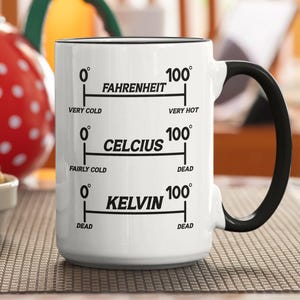 Puede incluir: Taza de cerámica blanca con asa y borde negros. La taza presenta escalas de temperatura en Fahrenheit, Celsius y Kelvin, con etiquetas como "Muy frío" y "Muy caliente".