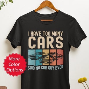 May include: Black t-shirt with a vintage-style graphic that says "I have too many cars said no car guy ever". The graphic features a row of three classic cars in a rainbow color scheme.