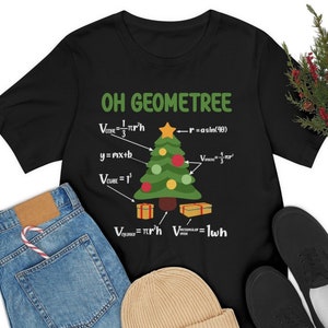 May include: Black t-shirt featuring a green Christmas tree and geometric formulas. The text on the shirt reads "OH GEOMETREE" and includes formulas for the volume of a cone, a cube, a cylinder, and a sphere. The formulas are written in white text.