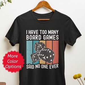 Puede incluir: Camiseta negra con un gr&aacute;fico de estilo vintage que dice "Tengo demasiados juegos de mesa, nadie ha dicho nunca eso". El gr&aacute;fico presenta una pila de dados con un fondo de arco&iacute;ris.