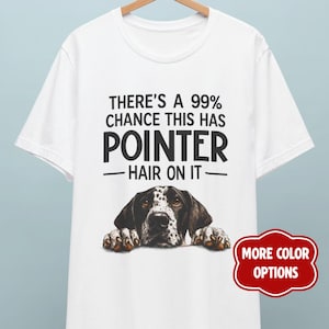 Könnte beinhalten: Ein weißes Kurzarm-T-Shirt mit einer Grafik eines Pointer-Hundekopfes, dessen Pfoten unten aufliegen. Der Text lautet: THERE'S A 99% CHANCE THIS HAS POINTER HAIR ON IT. Ein rotes Abzeichen auf der rechten Seite zeigt: MORE COLOR OPTIONS.