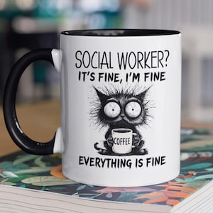 Może przedstawiać: Biały ceramiczny kubek z czarnym uchwytem i obramowaniem, z ilustracją kota trzymającego filiżankę kawy. Tekst na kubku brzmi: "SOCIAL WORKER? IT'S FINE, I'M FINE, EVERYTHING IS FINE."