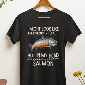 May include: Black t-shirt with a white graphic of a salmon fish and the text "I might look like I'm listening to you, but in my head I'm thinking about salmon."