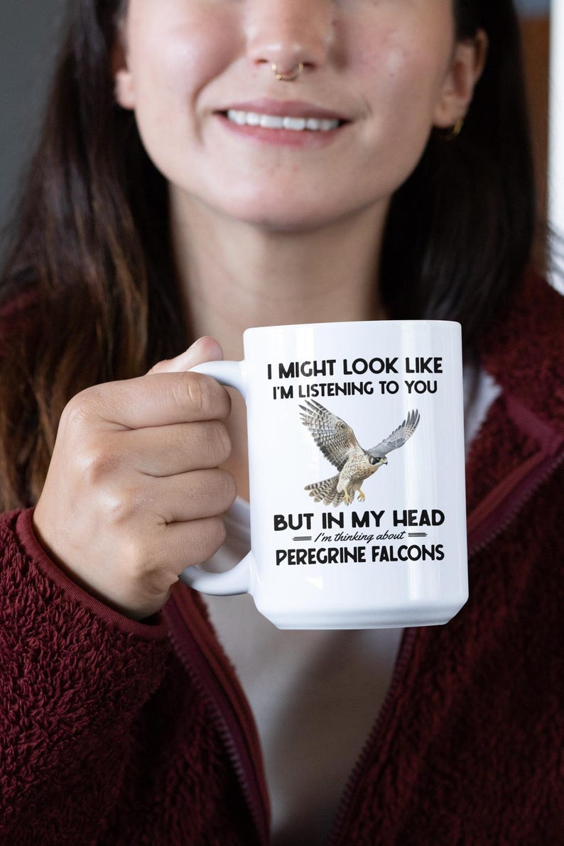 May include: White ceramic mug with a black graphic of a peregrine falcon in flight. The text reads "I might look like I'm listening to you, but in my head I'm thinking about Peregrine Falcons."