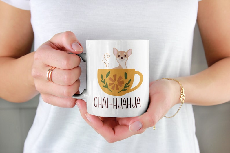 May include: White ceramic mug with a brown chihuahua sitting in a yellow teacup with a floral design. The text "Chai-huahua" is printed on the mug.