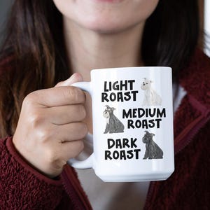 May include: White ceramic mug with a black and white illustration of a dog. The mug has the text "Light Roast", "Medium Roast", and "Dark Roast" with a dog illustration for each roast.