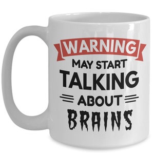 May include: White ceramic coffee mug with a black and red design. The text on the mug reads "WARNING MAY START TALKING ABOUT BRAINS".