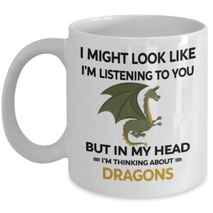 Puede incluir: Taza de caf&eacute; de cer&aacute;mica blanca con una ilustraci&oacute;n de drag&oacute;n verde y el texto "Puede que parezca que te estoy escuchando, pero en mi cabeza estoy pensando en dragones."