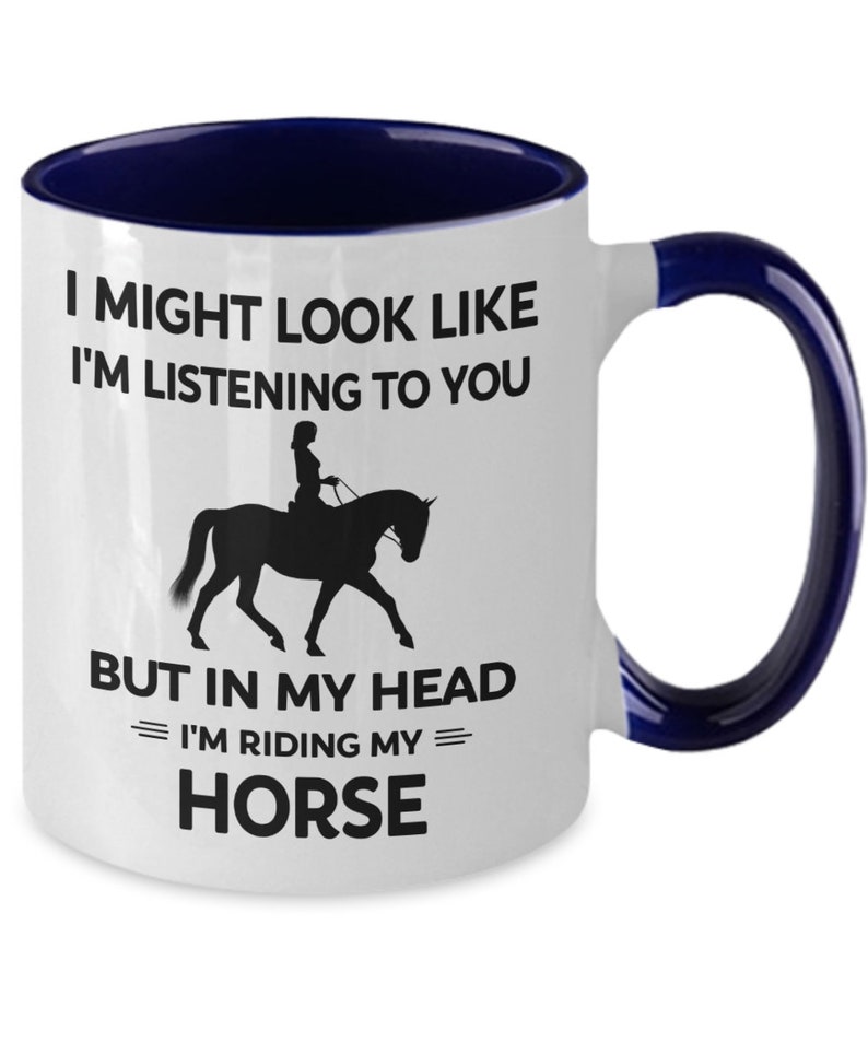 May include: White ceramic coffee mug with a blue rim and handle. The mug features a black silhouette of a person riding a horse with the text "I might look like I'm listening to you but in my head I'm riding my horse."