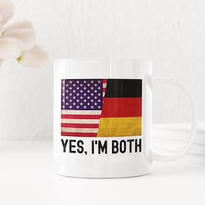 May include: White ceramic mug featuring a graphic of the American and German flags side-by-side. The text "YES, I'M BOTH" is printed below the flags.