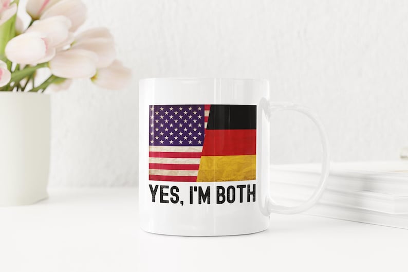 May include: White ceramic mug featuring a graphic of the American and German flags side-by-side. The text "YES, I'M BOTH" is printed below the flags.