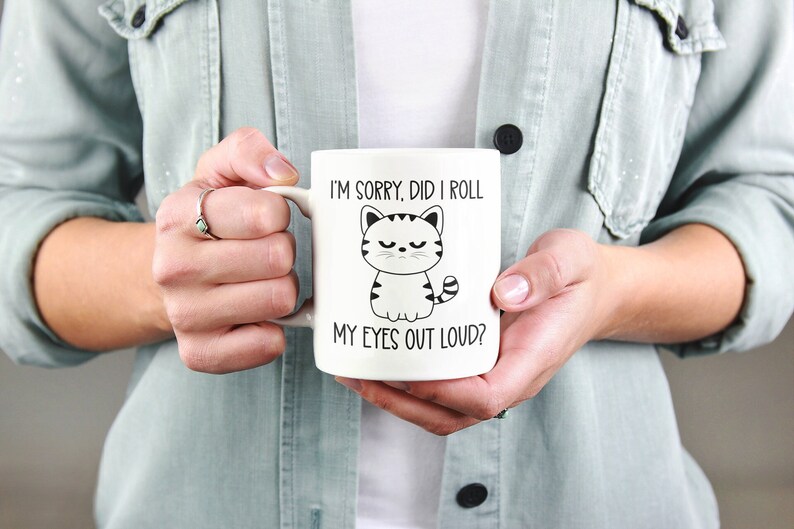 May include: White ceramic coffee mug with a black and white illustration of a cat with the text "I'm sorry, did I roll my eyes out loud?"