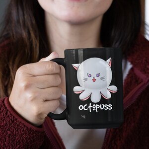 May include: A black coffee mug with a white octopus with pink tentacles and purple eyes. The octopus has a cat face and the text "octopus" is written below it.