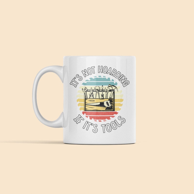 May include: White ceramic mug with a vintage-style graphic that reads "It's not hoarding if it's tools". The graphic features a toolbox with various tools inside, surrounded by a circular saw blade design.