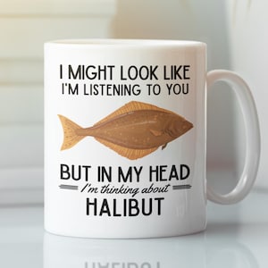 May include: White ceramic coffee mug with a black and white graphic of a halibut fish. The text on the mug reads "I might look like I'm listening to you but in my head I'm thinking about halibut."