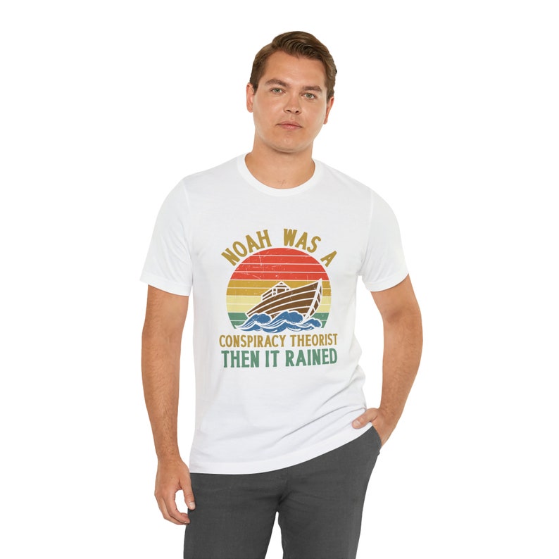 May include: White t-shirt with a vintage-style graphic of a boat on a wave with the text "Noah was a conspiracy theorist then it rained".