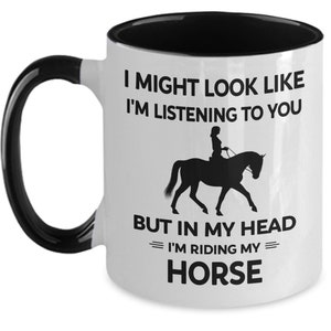 May include: White ceramic coffee mug with a black interior and handle. The mug features a black silhouette of a person riding a horse with the text "I might look like I'm listening to you but in my head I'm riding my horse."