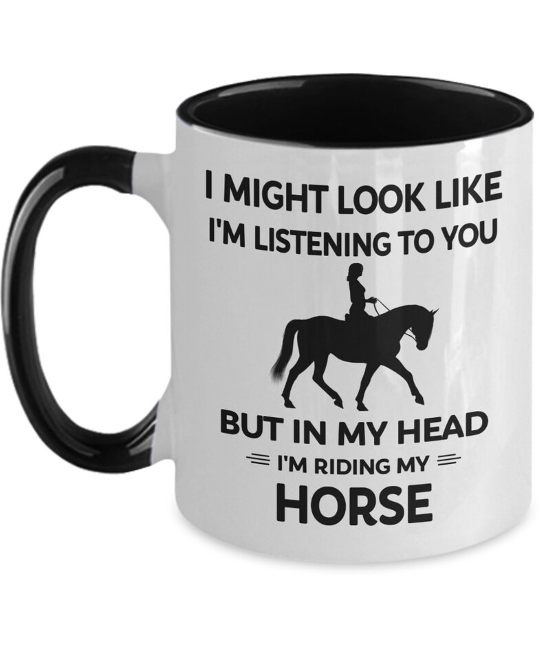 May include: White ceramic coffee mug with a black interior and handle. The mug features a black silhouette of a person riding a horse with the text "I might look like I'm listening to you but in my head I'm riding my horse."