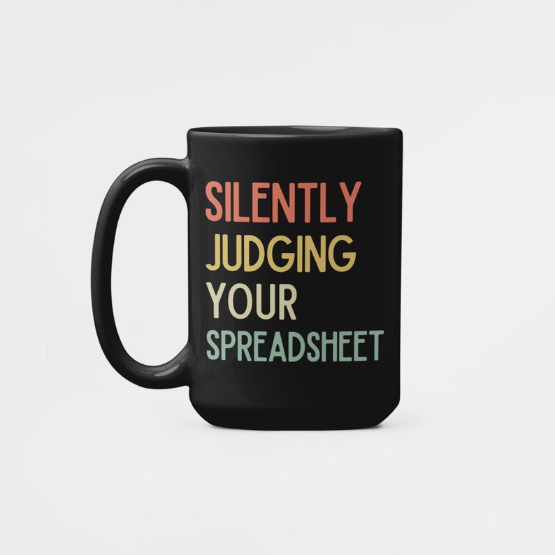K&ouml;nnte beinhalten: Schwarze Kaffeetasse mit dem Text "SILENTLY JUDGING YOUR SPREADSHEET" in einem Retro-Farbschema.