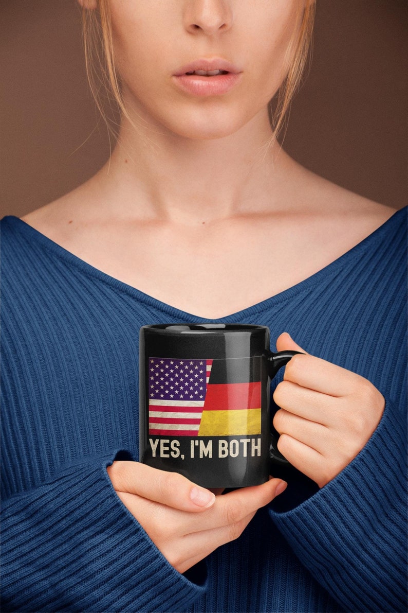 May include: Black coffee mug with a white and red American flag and a black, red, and yellow German flag on the front. The text "YES, I'M BOTH" is printed below the flags.
